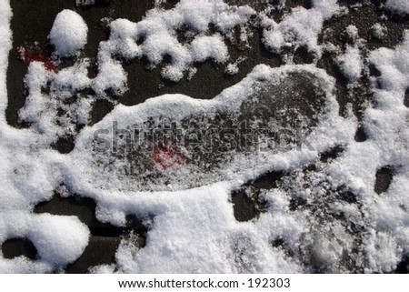 Semi-melted footprint in snow on painted pavement; edges have hardened as weather thawed & froze