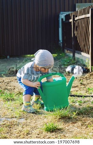 little boy plays with a watering can in the garden, next to the greenhouse