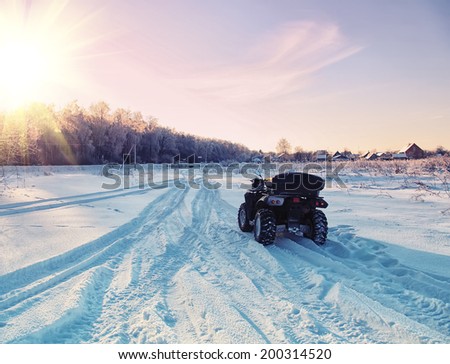 quad bike on a winter road in a field at sunset. focus on quad bike.