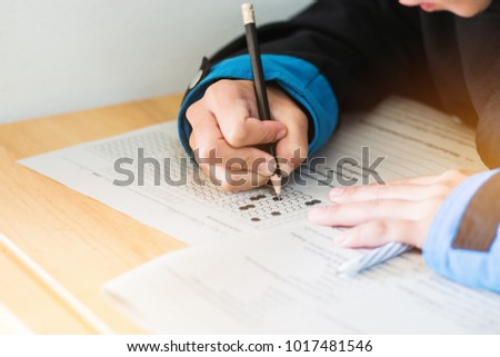 high school or university student hands taking exams, writing examination on paper answer sheet optical form of standardized test on desk doing final exam in classroom. Education  literacy concept.