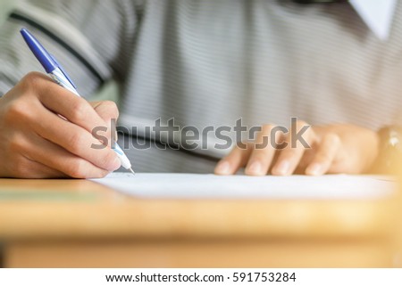students hand holding pen fill in Exam carbon paper sheet or test paper on wood desk