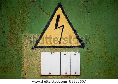 Yellow high voltage sign on aged green textured wall. Empty white sign board below for some text