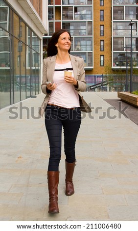 young woman walking with phone and coffee.