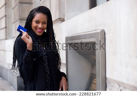 a happy young woman holding a cash card at a cash mashine.
