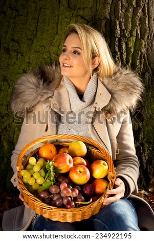 young woman sitting in a park with a basket of fruit.