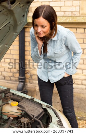 young woman broken down looking curiously at the engine.