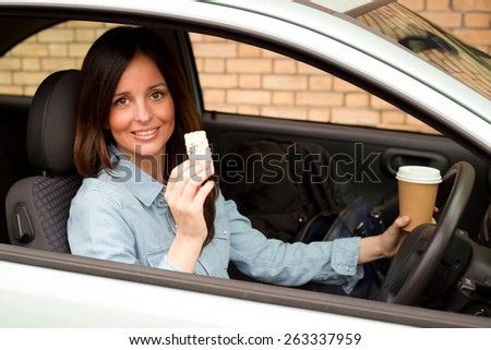 a young woman having a healthy snack and coffee in her car