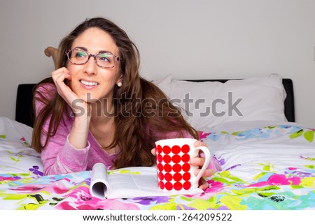 young woman thinking in bed with a coffee and magazine
