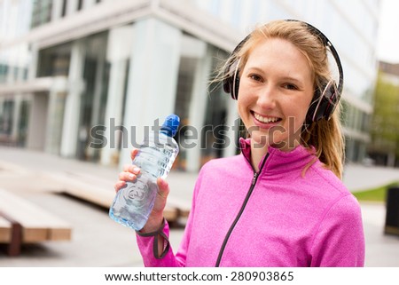 young woman wearing headphones and holding water bottle.