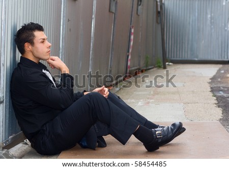 a young man reflecting on his life sitting on the floor.