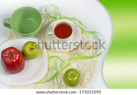 Refined card with a still life in complementary colors - green and red on a white background. Apples, plates, cup of tea, candies and green satin ribbons on a straw napkin.