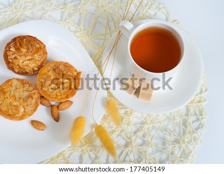 Almond cakes with nuts covered with glaze on plate near cup of tea and sugar slices.