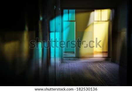 Narrow dark corridor in ancient building with set of doors. Two doors are open and from them bright light flows, color patches of light shine walls and floor.