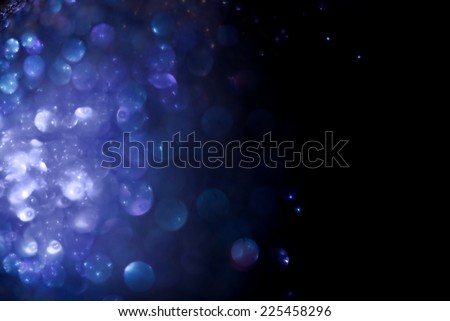 Sparkling abstract blue background. Bright indistinct patches of light of different shades of blue color on  black background.
