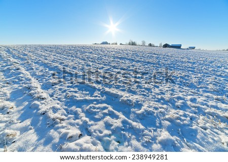 Village on hill and plowed field under snow.