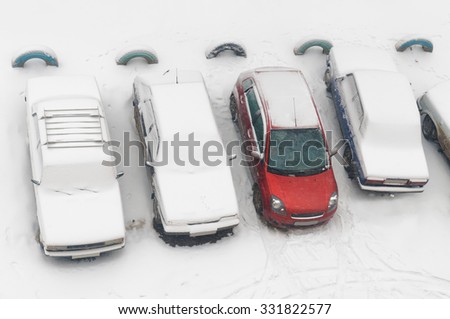 Rub cars completely covered with snow and one red car partially dug out on parking in the city yard during snowfall.
