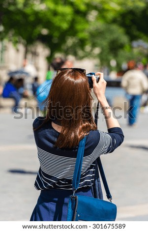 Back side of a young woman taking a photo with her camera in Paris