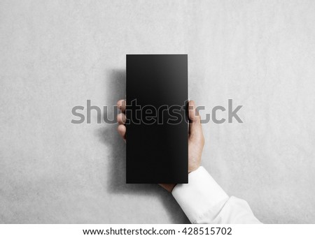 Hand holding blank black flyer brochure booklet in the hand. Leaflet presentation. Pamphlet hold hand. Man show grey offset paper. Sheet template. Booklet design. Paper sheet display read first person