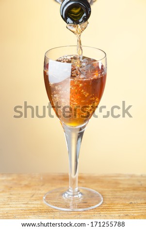 photo of glass of orange wineb on wooden table being poured from bottle on warm background.selected focus used