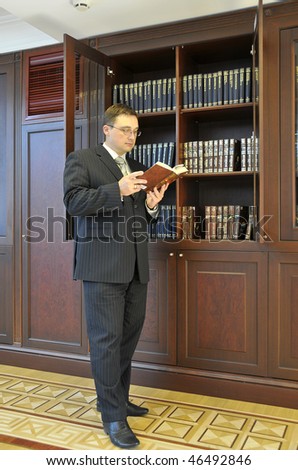 A man is standing near the shelves and read the book