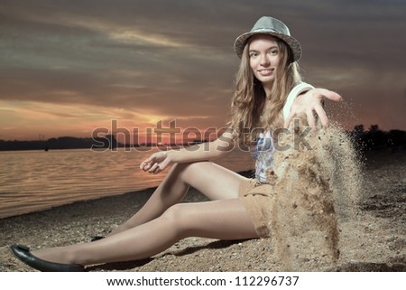 The girl sits on a beach and throws sand