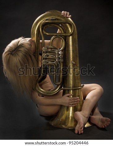 The girl sits with the big wind instrument on a black background