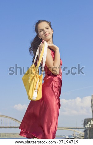 The girl in a red dress, with a yellow bag against the sky