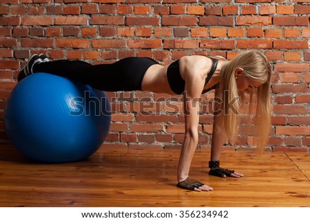 Attractive blond fitness model performing push ups with a fitball at the gym