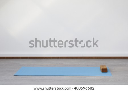 Mat and supporting unit for yoga and fitness lying on the floor. The room is flooded with daylight sunlight from the window, the glare on the white wall.