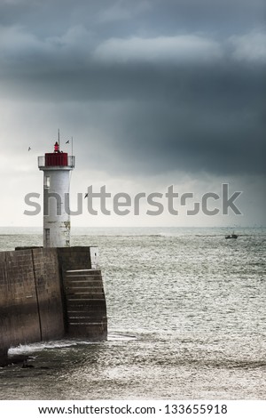Lighthouse at the end of the mole, and fishing boat, far at the sea, France, atlantic ocean