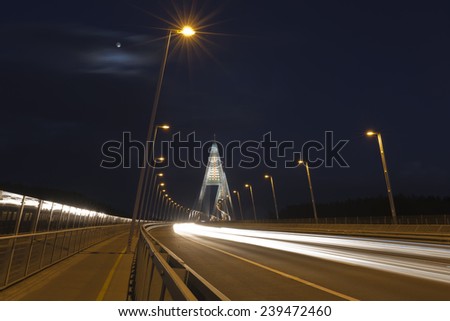 Lights on a modern bridge, street lights, moving cars and the moon too.