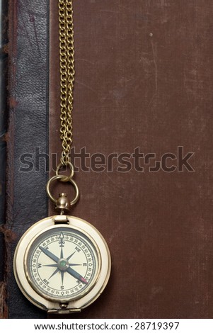 old brass compass with rusted antique book with leather back on the background