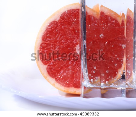 Juicy red grapefruit and a glass of mineral water on a white background.
