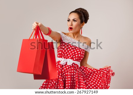 Funny portrait of a smiling cute young female model holding many shopping bags in her arms wearing red dress