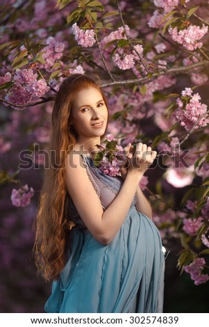 Beautiful pregnant woman smells blossom, outdoor in nature.
