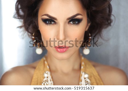 Beautiful woman with evening make-up and curly hair and yellow dress with jewelry pearls. Smoky eyes. Fashion portrait photo. Picture taken in the studio over bokeh shiny circles background.