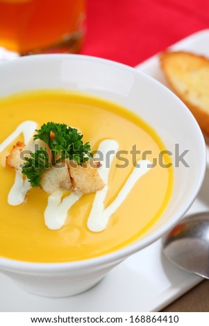 The bowl of pumpkin soup and bread in dish on the table.