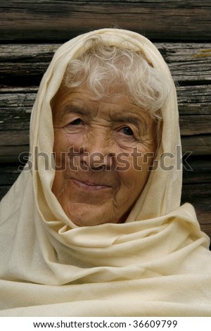 Charming old woman wrapped in a beige scarf. She is smiling and looking very happy.