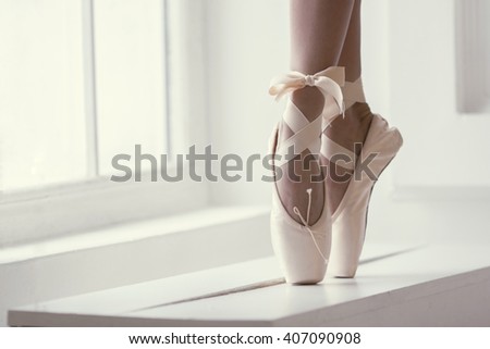 Legs of a ballerina in pink pointe shoes with a bow are dancing near the window