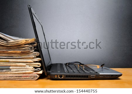 Laptop and newspapers on a table with black background