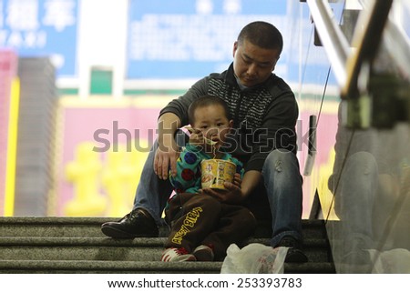 GUANGZHOU, CHINA - FEB. 14. 2015: Father and son eats on plateau of Gunagzhou Main Railway Station while waiting for the train in Guangzhou, Guangdong province.