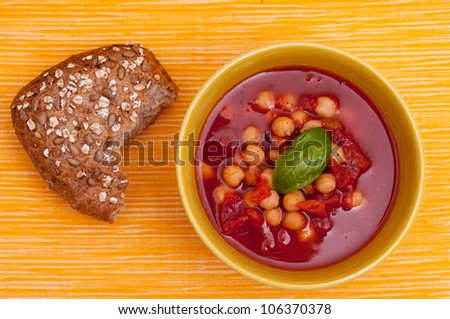 Wholemeal roll with red vegetable soup in a yellow bowl and background