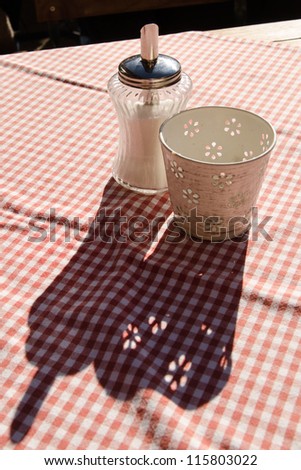 Sugar dredger on a white red table cloth in the backlit