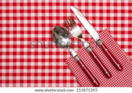 Cutlery with red knife, fork and spoon on red checked napkin and table cloth
