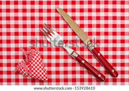Knife and fort with red checkered heart and bow on table cloth