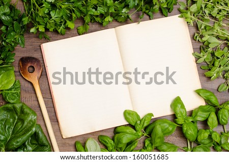 Book for recipes with wooden spoon and green herbs