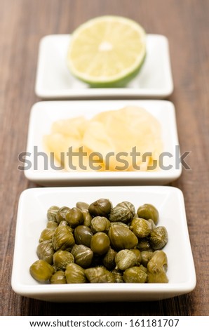 Capers, ginger and lime in a bowl in vertical format