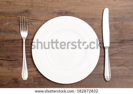 White plate with silver knife and fork on a wooden board