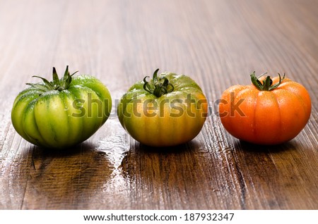 Green and red tomatoes on a wooden table, with water drops