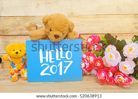 Teddy bear with red and pink flower on wooden floor and Hello 2017 note on morning sunlight. vintage color tone, Hello 2017 concept.